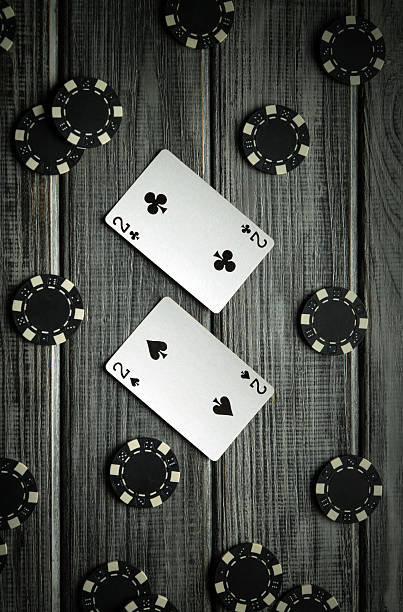 istock Two playing cards, both twos, lie between several black poker chips on a rustic wooden table. It highlights a vibrant game atmosphere during a casual gathering at night 2220557865