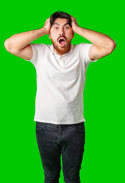 istock A man with a surprised expression holds his face while against a vibrant green background 2220562048