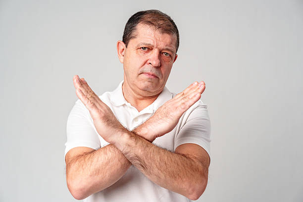A man making a gesture of refusal with arms crossed against a light background