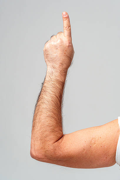 Hand raised with index finger pointing upward against a plain light background close up