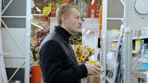 istock Man carefully choosing light bulb in hardware store, comparing options for home improvement project. Focus on energy efficiency and product details 2220587530