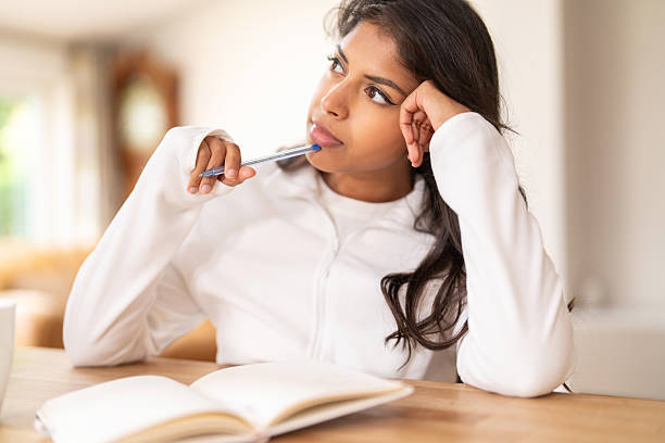 istock Thoughtful young woman reflecting while studying indoors with a notebook and pen in a cozy, well-lit environment during the day 2220588617