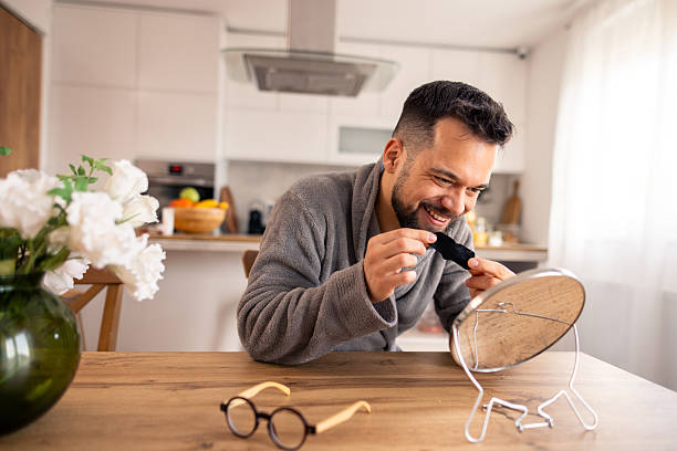 istock Smiling Caucasian Man in Grey Robe Applying Cream to Face in Bright Kitchen 2220591258