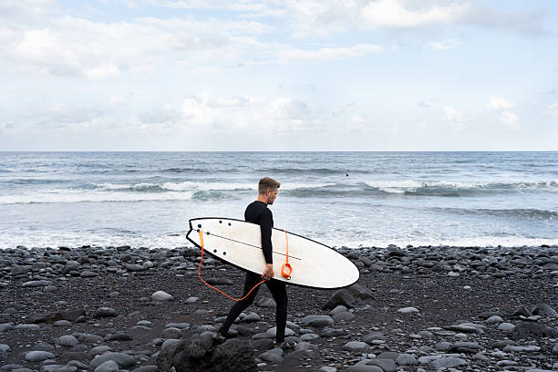 Surfer walking on the beach with his surfboard under his arm, getting ready to surf the ocean waves