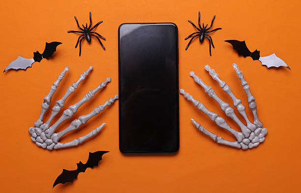 istock Halloween decoration concept. Plastic skeleton hands and smartphone on orange background 2220593786