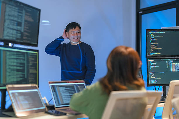 istock young Asian software development manager leads a late-night office discussion with his executive team, mentoring developers and analyzing source code to guide programming and project development 2220599044