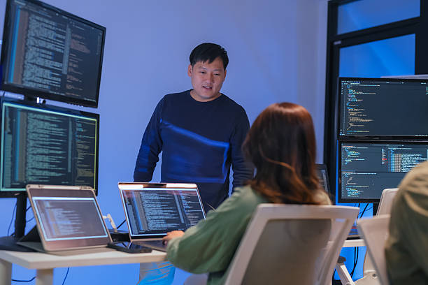 istock young Asian software development manager leads a late-night office discussion with his executive team, mentoring developers and analyzing source code to guide programming and project development 2220599127