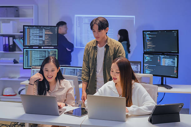 istock young Asian software development manager leads a late-night office discussion with his executive team, mentoring developers and analyzing source code to guide programming and project development 2220599206