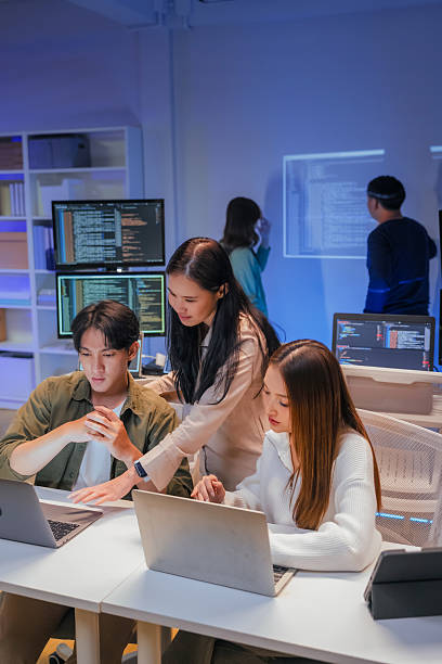 istock young Asian software development manager leads a late-night office discussion with his executive team, mentoring developers and analyzing source code to guide programming and project development 2220599210