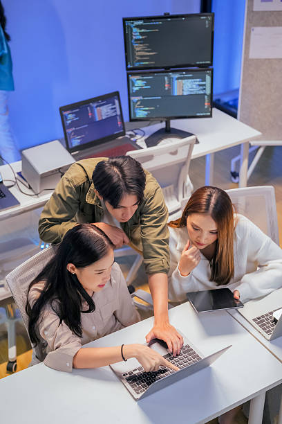 young Asian software development manager leads a late-night office discussion with his executive team, mentoring developers and analyzing source code to guide programming and project development