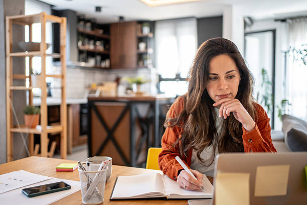 istock Focused businesswoman working from home taking notes in notebook 2220599876