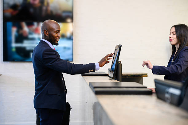 istock Side view of a business man in a suit using a touchscreen computer to check in at a modern hotel reception desk 2220603042