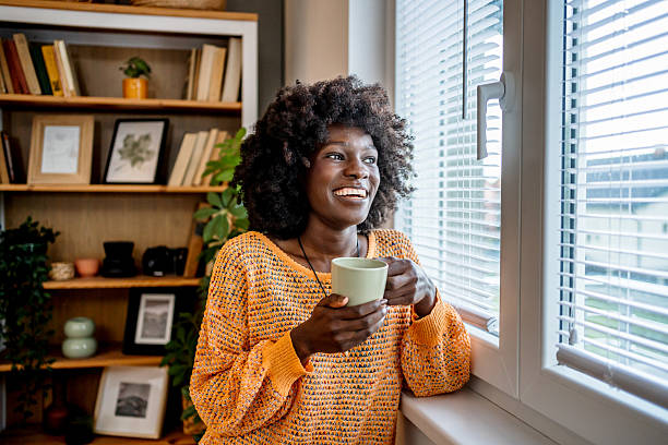 istock Smiling black woman drinking coffee and looking out the window 2220603183