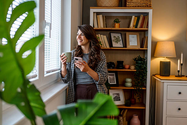 istock Young woman enjoying morning coffee and using smartphone by window 2220603342