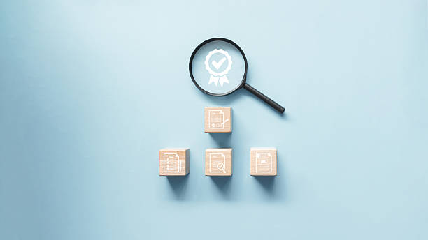 istock Magnifying glass on certificate icon and wooden block with document icon on it. Concept of document management for quality control check and quality assurance certification. 2220611310