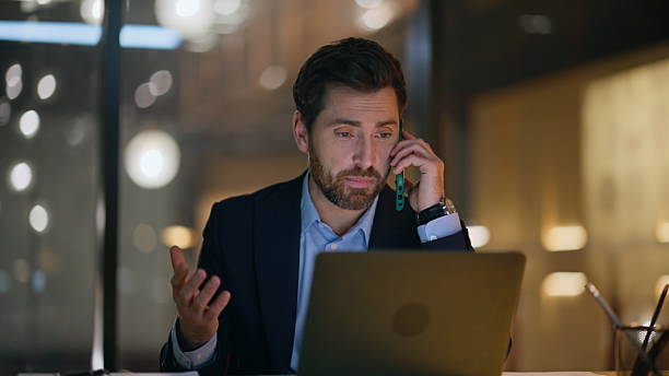 istock Hardworking manager talking mobile phone looking laptop at dark office closeup. 2220611531