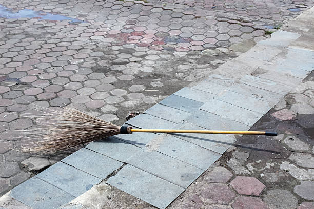 A traditional broomstick is placed on a sidewalk with textured paving. This photo depicts a traditional Indonesian cleaning tool used to sweep up leaves or dirt in outdoor areas. Taken with natural daylight, it gives a simple and authentic atmosphere.