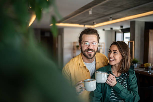 istock Happy couple smiling and drinking coffee in their modern apartment 2220612330
