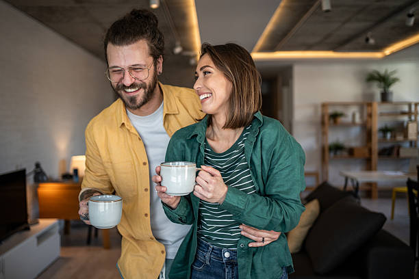 istock Happy couple laughing and drinking coffee in modern apartment 2220612344