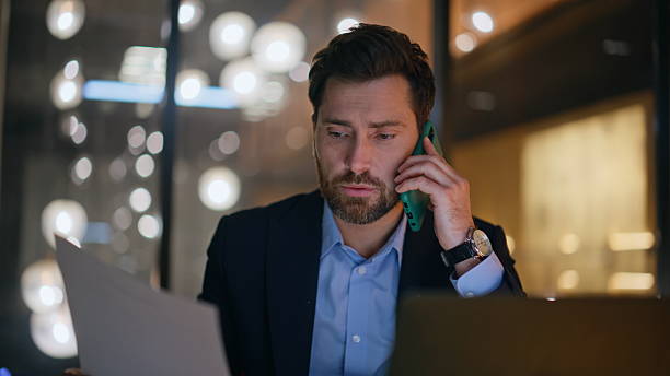 istock Confident boss talking mobile phone reviewing papers at night workplace closeup. 2220613410