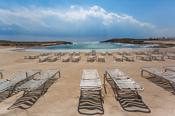 Rows of empty sunbeds stand on a sandy beach, inviting tourists to relax by the clear turquoise water
