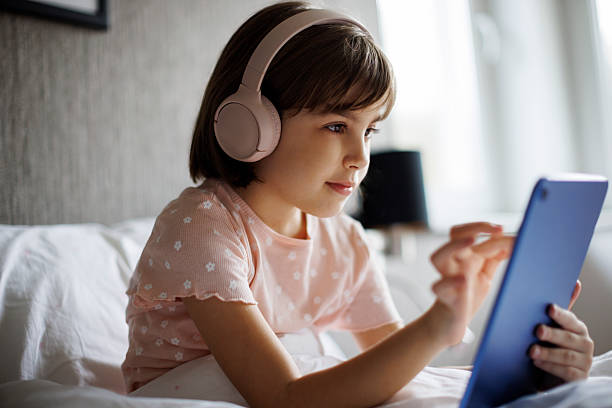 istock Cute little girl using digital tablet in bed 2220618585