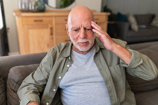 istock Senior man having headache frowning on couch at home 2220620156