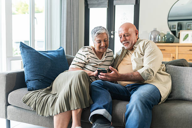 istock Cheerful senior couple using cellphone on couch at home 2220620237