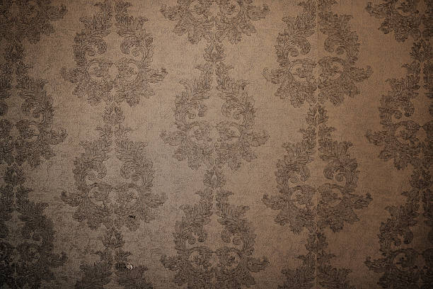 Old vintage wallpaper with a complex repeating pattern in muted beige tones, with significant wear and scratches in places
