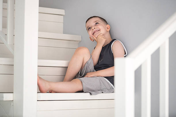 A young boy sitting on indoor stairs, smiling and engaged in thought. The scene showcases a minimalist setting, reflecting innocence and creative contemplation.