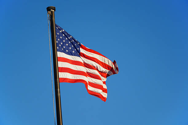 istock waving USA flag on pole against blue sky 2220623645