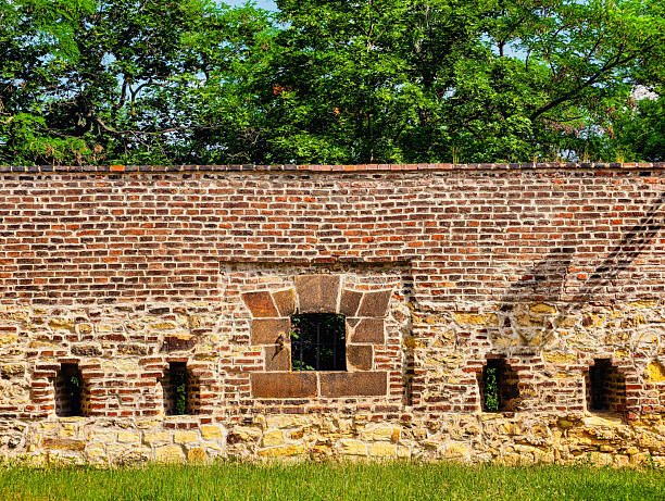 Historic Embrasures: Glimpse of a Medieval Fortress Wall – Captivating Brick Structure with Openings for Defense, Surrounded by Lush Greenery and Beautiful Blue Sky, Perfect for Travel Enthusiasts