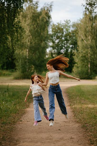 Two sisters running on dry autumn leaves in a beautiful forest during a sunny fall day