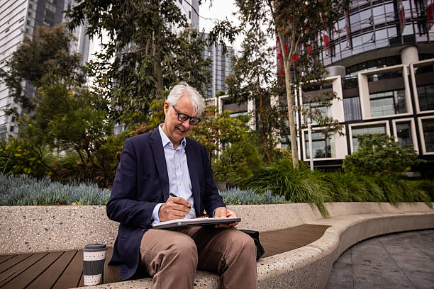 istock Elderly Businessman Planning Work on Bench in Downtown Sydney 2220629633