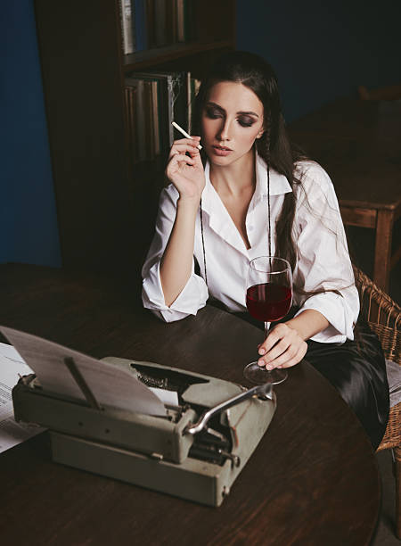 istock Writer (journalist) typing on old typewriter, smoking cigarette and drinking wine. Indoors old-fashioned portrait of pretty young girl. Retro (vintage) style 2220633466