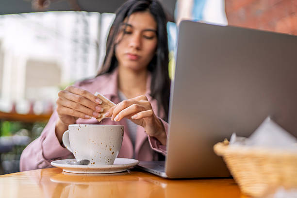 istock Freelancer pouring sugar in a cup of coffee while working from a coffee shop 2220636681