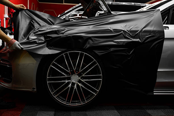 istock Matte black vinyl is applied across car hood. Car wrapping process using black matte vinyl stretched into place. Careful application and tensioning of black vinyl avoids surface damage or bubbling. 2220636988