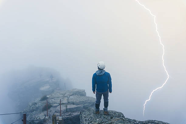 Hiker standing on the summit of cofre de perote volcano in veracruz, mexico, watching a lightning strike during a foggy day