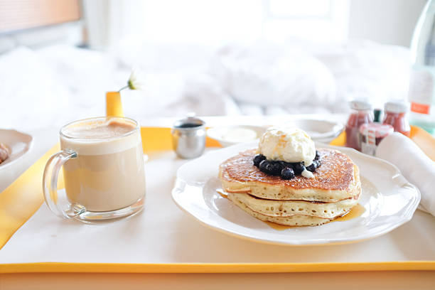 Room Service tray with pancakes and cappuccino with bed in background in New York, New York, United States