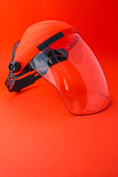 istock Protective face shield with transparent visor and orange headgear, isolated on bright red background, used for safety during industrial, construction or gardening work 2220650352