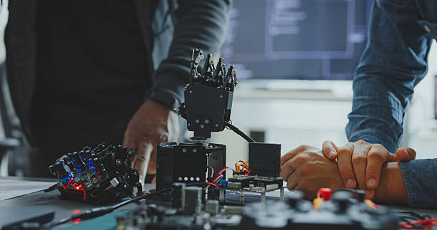 istock Closeup of Black and Hispanic male engineers programmers work together on robot hand prototype, use computer control robotic arm circuit in tech office. Software developer, artificial intelligence. 2220652761
