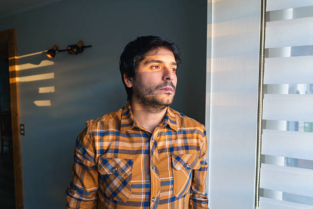 istock Pensive man looking out of window in sunlight 2220653431