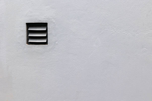Gray wall with small ventilation grate on minimalist surface.