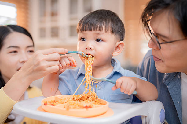 istock Family enjoys mealtime as toddler eagerly eats spaghetti in a bright kitchen setting 2220668343