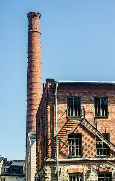 istock Tall red brick chimney and industrial building in sunlight against blue sky 2220675015