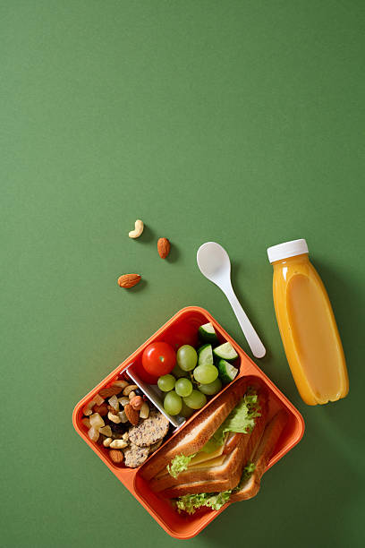 Healthy lunchbox with sandwich, fruits and nuts on green background
