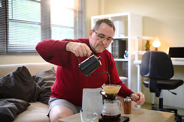 istock Senior man in red sweater making pour over coffee at home with a focused expression 2220677710