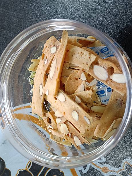 Almond sliced cookies in a transparent bowl on a dark background, top view