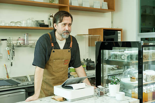 istock Male waiter stands behind the cafe counter, smiling warmly while adding a friendly and welcoming atmosphere to the relaxed retirement gathering., Concept small business 2220680073