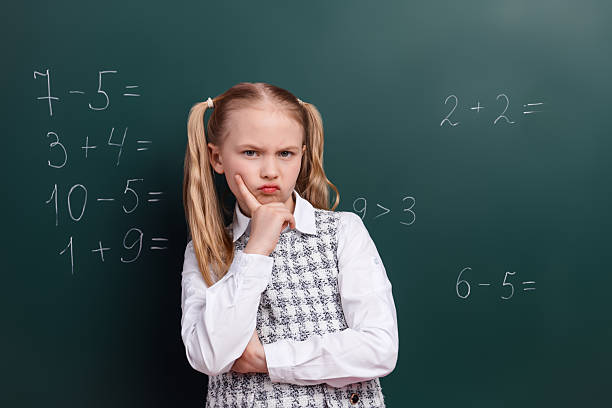 istock Thoughtful schoolgirl in uniform ponders math problems on chalkboard during classroom lesson in education setting 2220681648